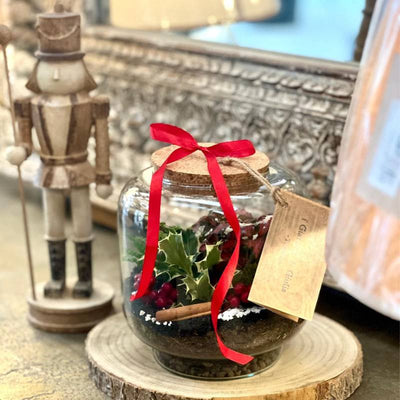 terrarium in vetro con piante con fiocco rosso su base in legno con soldatino Natale di fianco