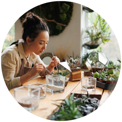 Donna intenta a creare un terrarium artigianale con piante verdi su un tavolo di legno luminoso.