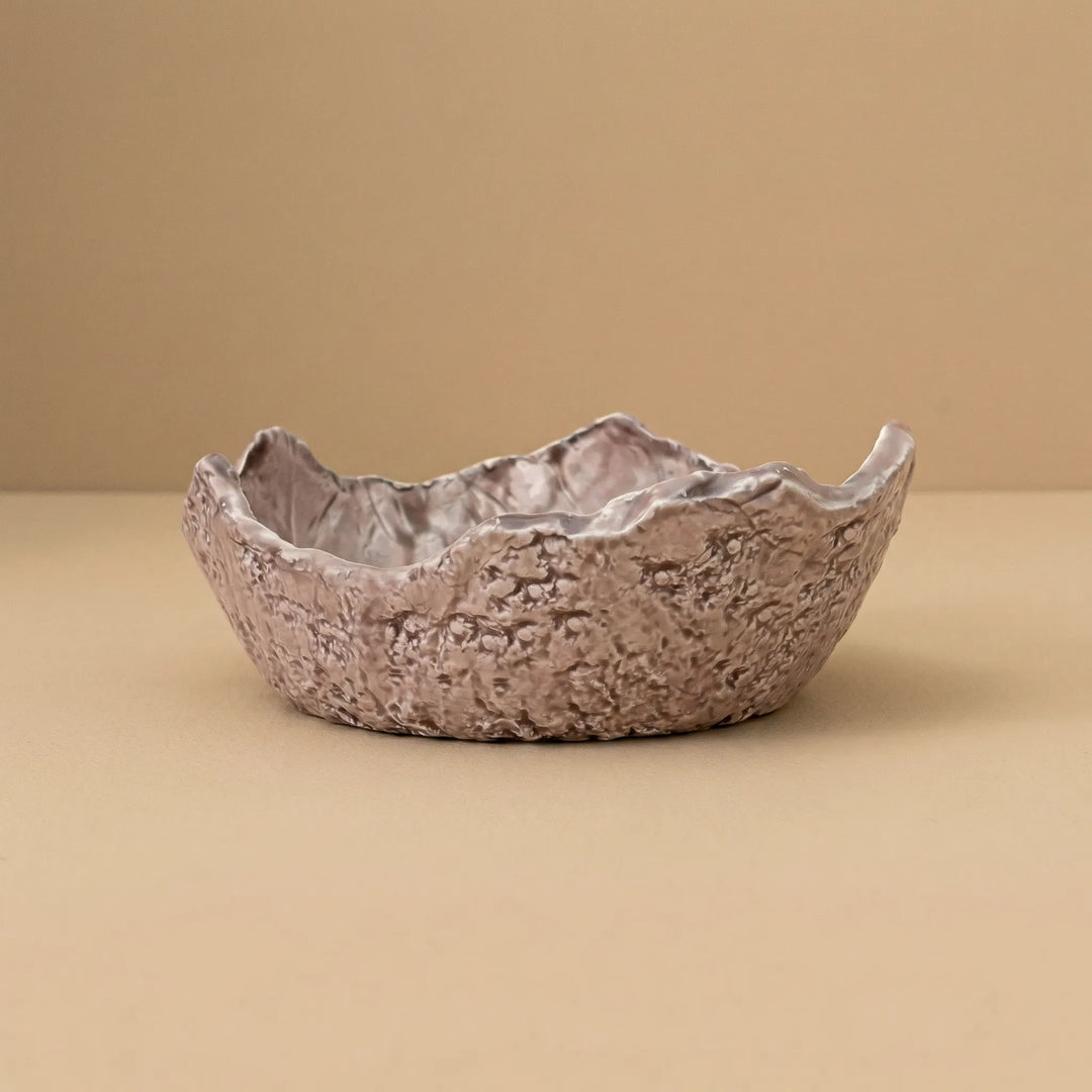 Ciotola in ceramica artigianale con bordo irregolare e texture naturale su sfondo neutro beige