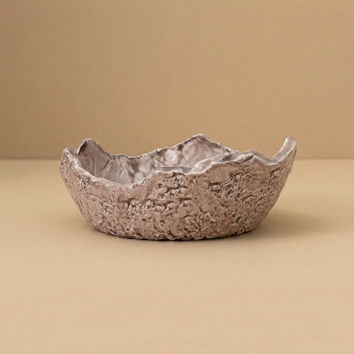 Ciotola in ceramica artigianale con bordo irregolare e texture naturale su sfondo neutro beige