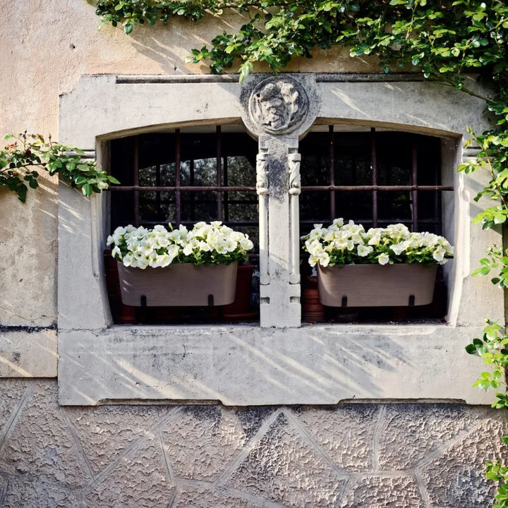 Due fioriere Paros installate su davanzale esterno con petunie bianche in fiore, ideali per decorare finestre e facciate.