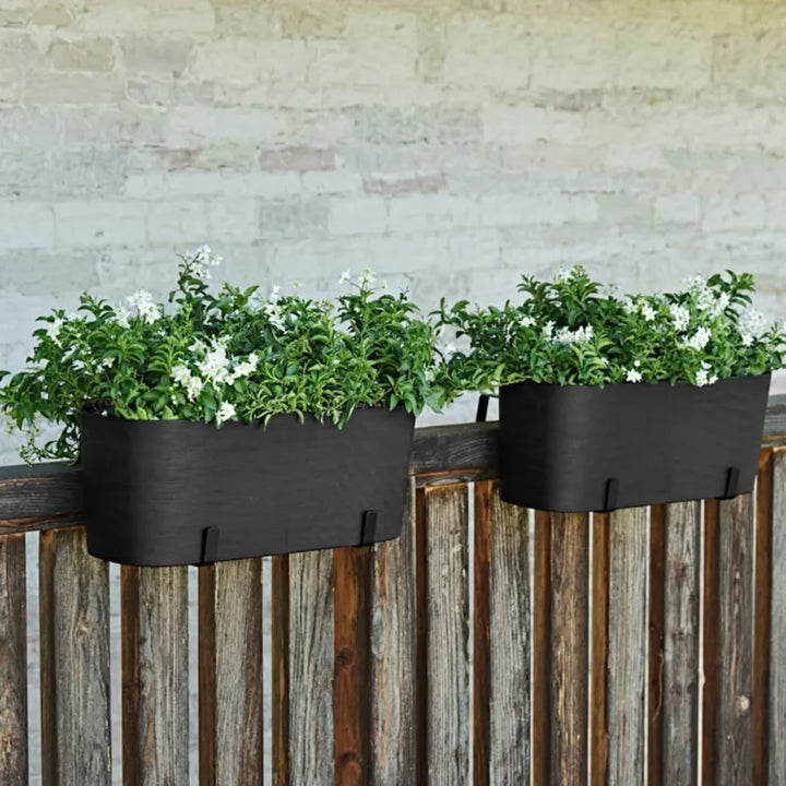 Coppia di fioriere Paros nere installate su una recinzione in legno con piante a fiore bianco dall'aspetto elegante e contemporaneo.