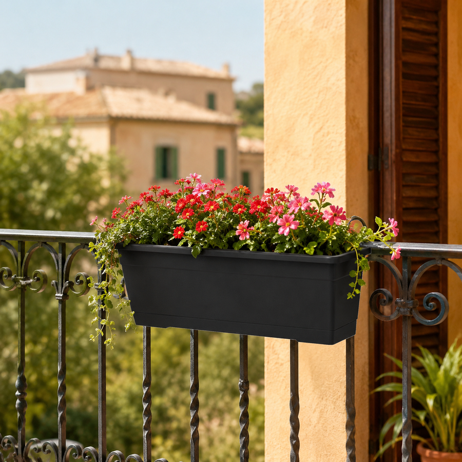 Fioriera Birka nera fissata alla ringhiera di un balcone, coltivata con fiori rosa e rossi ricadenti, perfetta per decorare terrazzi e balconi soleggiati.