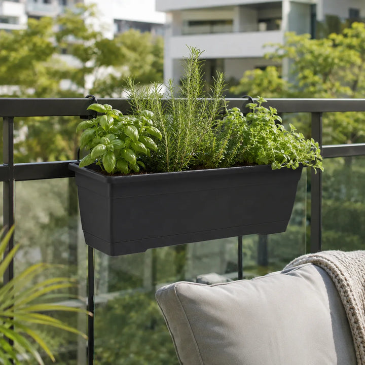 Fioriera Birka nera con basilico, rosmarino e altre erbe aromatiche coltivate su una ringhiera moderna, ideale per creare un orto urbano sul balcone.