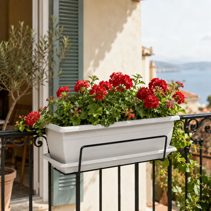 Fioriera Nara bianca installata su ringhiera con gerani rossi in fiore, ideale per decorare balconi e terrazzi.