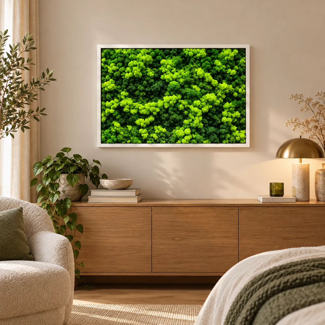 Quadro di licheni stabilizzati 83x63 cm con cornice bianca, composizione verde tridimensionale, appeso sopra un mobile in legno in soggiorno luminoso.