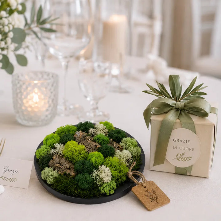 Quadro tondo nero in muschio e licheni stabilizzati inserito in un elegante allestimento con confezione regalo, candele e decorazioni floreali naturali.