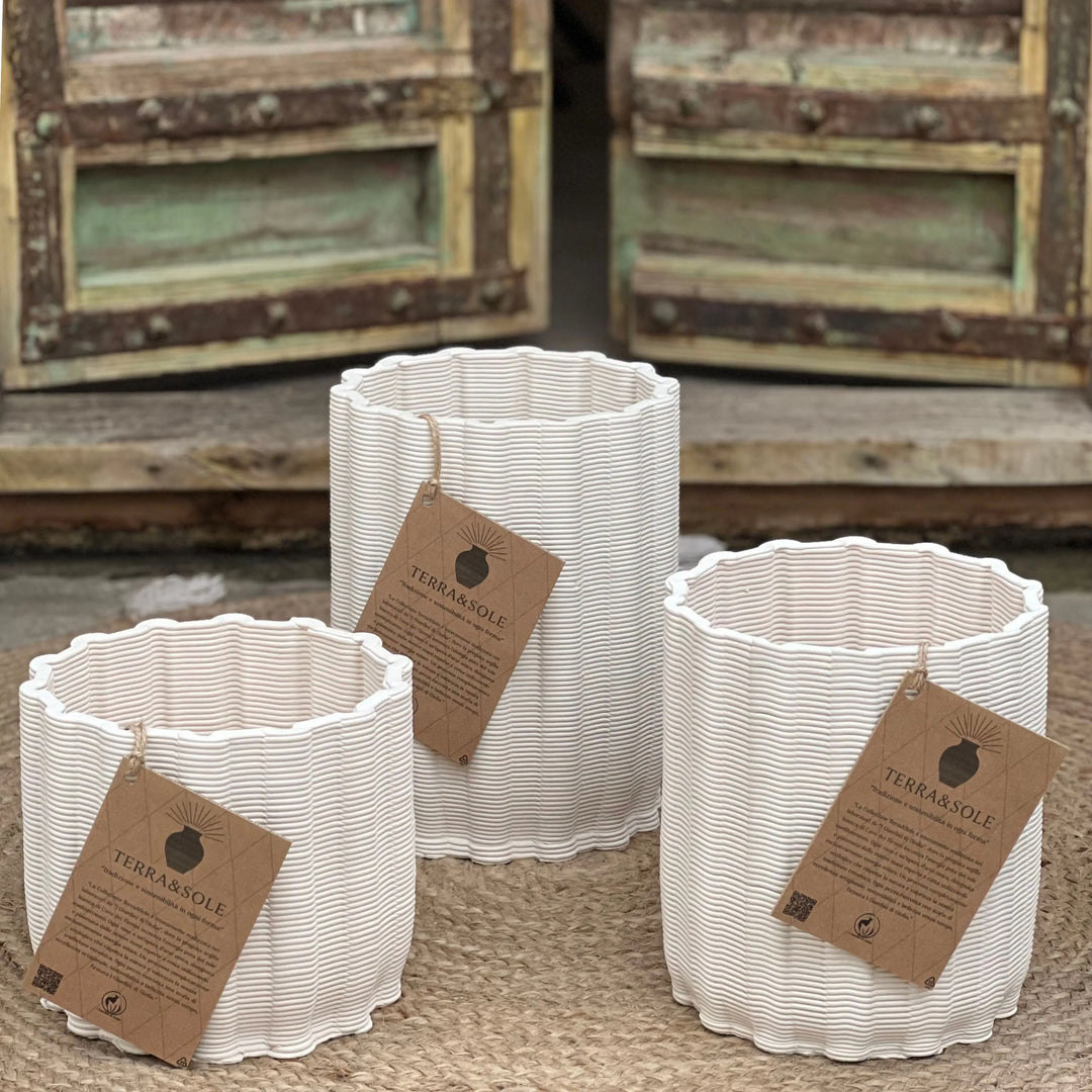 Set di tre vasi Giulia in argilla bianca naturale con etichette Terra&Sole, disposti su tappeto in fibra davanti a portone rustico.