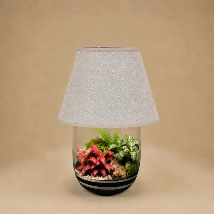 Terrarium artigianale Oasi Lux Elegant con piante tropicali da interno racchiuse in una lampada decorativa con paralume beige e vaso in vetro.