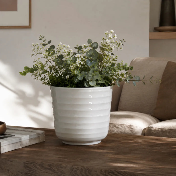 Vaso Cindy bianco con composizione di eucalipto e piccoli fiori bianchi, posizionato su tavolo in soggiorno dallo stile elegante e contemporaneo.