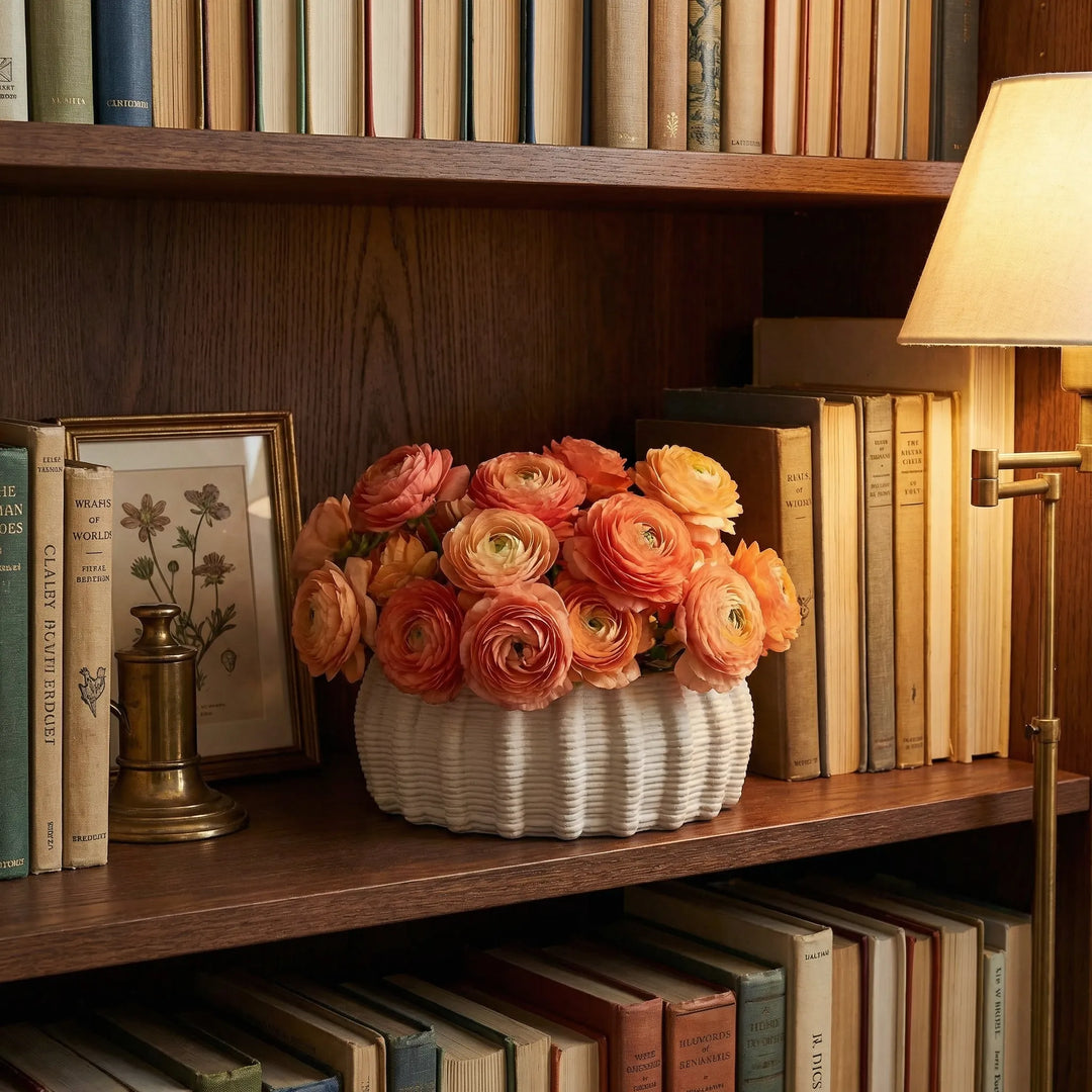 Vaso in ceramica artigianale Dioniso con ranuncoli arancioni su mensola tra libri e lampada