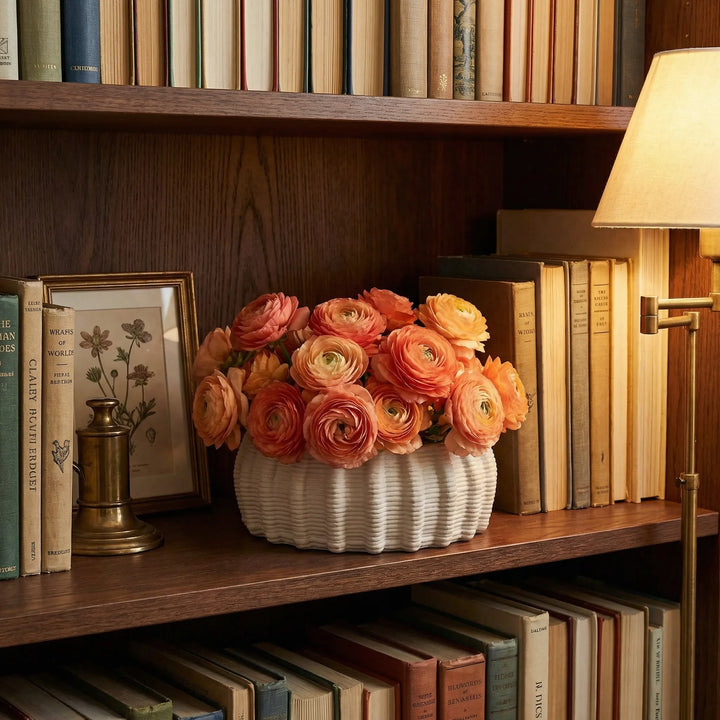 Vaso in ceramica artigianale Dioniso con ranuncoli arancioni su mensola tra libri e lampada