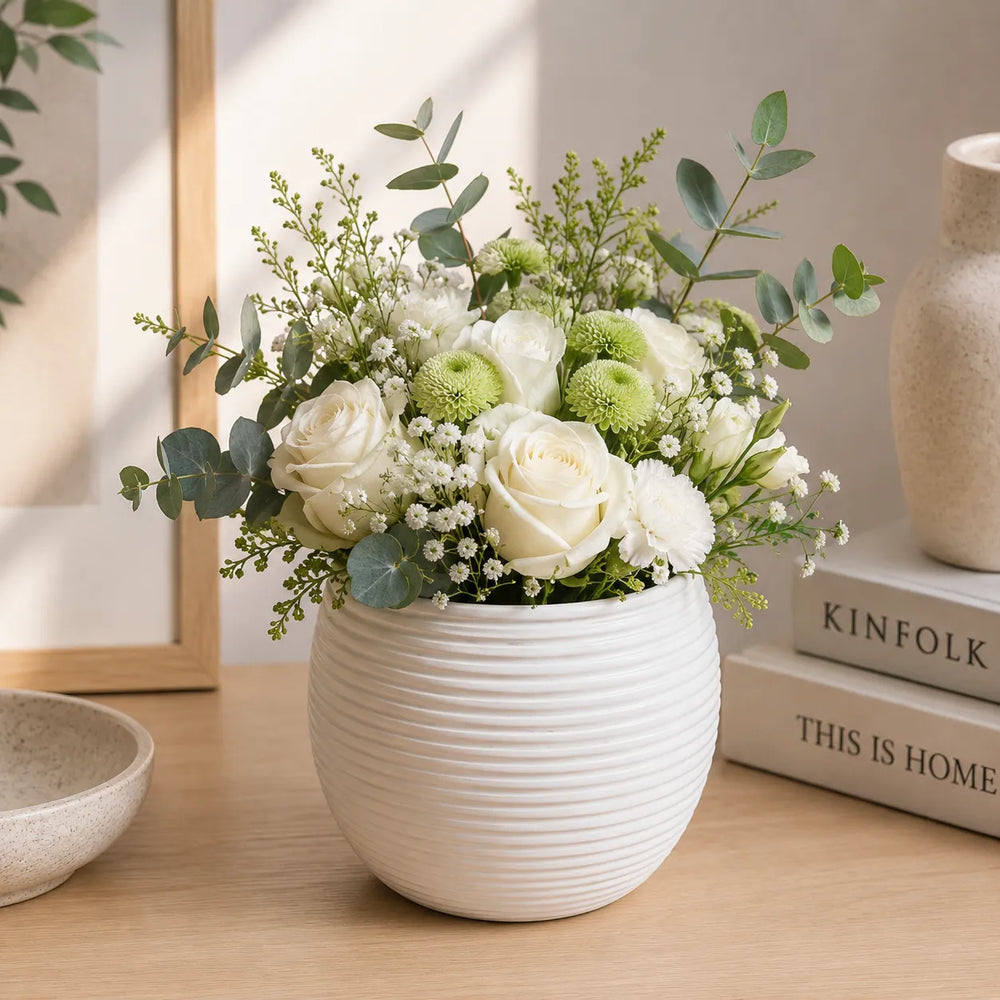 Vaso Sally bianco in ceramica con composizione floreale di rose bianche, crisantemi verdi, eucalipto e fiori decorativi, ideale come centrotavola elegante per la casa.