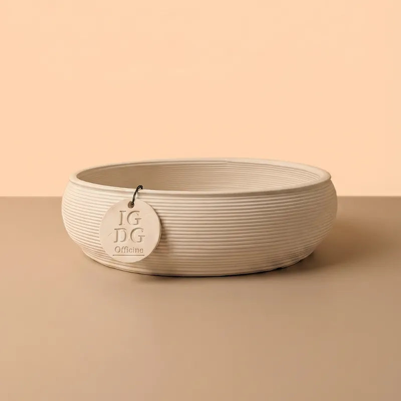 Vaso ovale in ceramica artigianale beige con superficie rigata su sfondo neutro