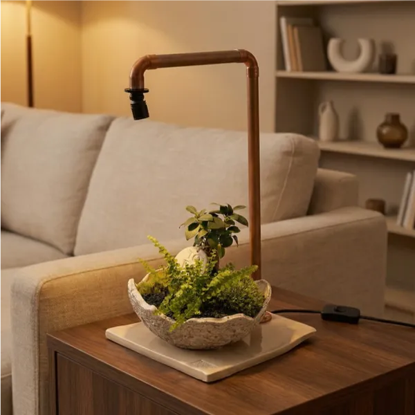 Lampada LED in tubo di rame con composizione bonsai Ficus, felce capelvenere e muschio in ciotola ceramica artigianale su tavolino in noce in soggiorno moderno con luce calda