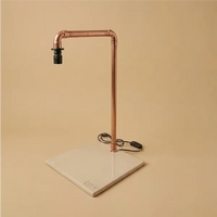 Lampada LED da tavolo industriale in tubo di rame con base quadrata in ceramica artigianale color crema, interruttore a filo nero su sfondo beige