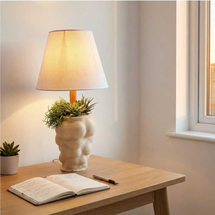 Lampada da tavolo con vaso design e composizione di piante grasse decorative su scrivania in legno vicino alla finestra.