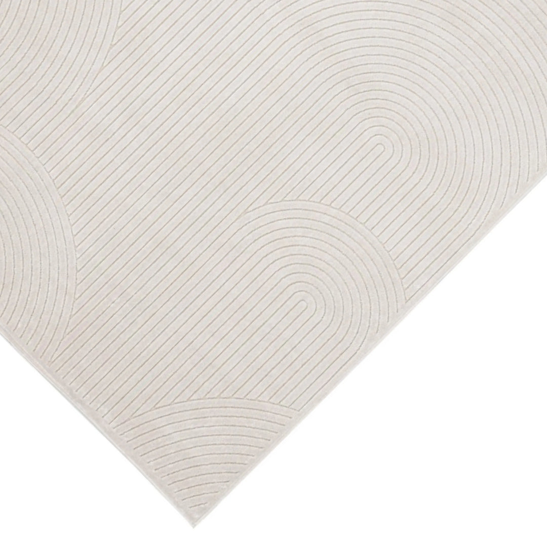 Dettaglio dell’angolo del tappeto moderno avorio con rilievo geometrico a righe curve, su sfondo chiaro.