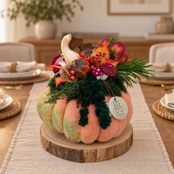 Composizione autunnale in zucca vera, con verde stabilizzato e base in legno, al centro di una tavola con runner chiaro.